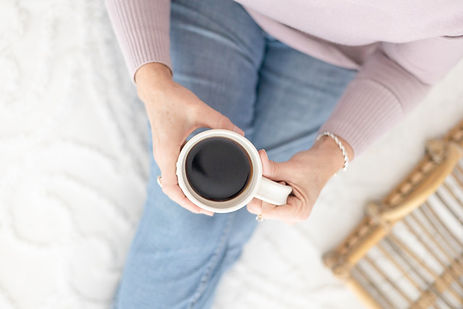 Woman sitting on a bed holding a cup of coffee, viewed from above. Woman sitting on a bed holding a cup of coffee, viewed from above.