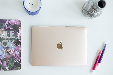 Closed laptop on a white desk with a notebook, coffee cup, vase, and colorful pens. Closed laptop on a white desk with a notebook, coffee cup, vase, and colorful pens.