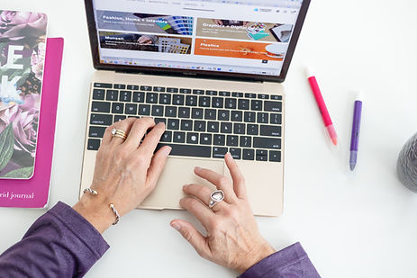 Person working on a laptop at a desk with colorful pens and a floral notebook. Person working on a laptop at a desk with colorful pens and a floral notebook.