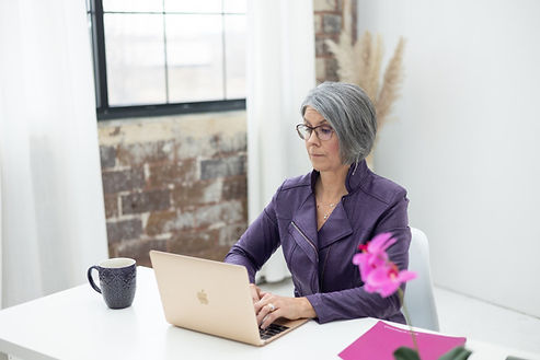 Woman in a purple jacket working on a laptop at a desk with a coffee cup and flowers. Woman in a purple jacket working on a laptop at a desk with a coffee cup and flowers.