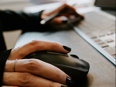 Close-up of a person using a computer mouse beside a laptop. Close-up of a person using a computer mouse beside a laptop.