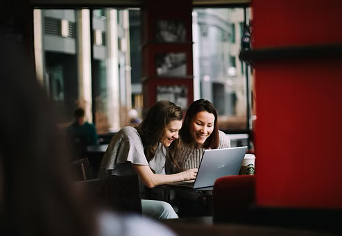 Two women collaborating on a laptop while seated in a café. Two women collaborating on a laptop while seated in a café.
