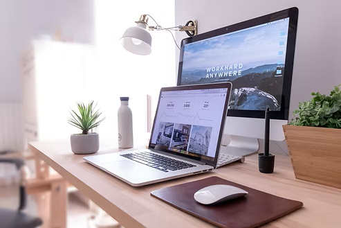 Modern workspace with a laptop, desktop monitor, wireless mouse, and potted plants. Modern workspace with a laptop, desktop monitor, wireless mouse, and potted plants.