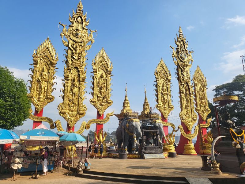 The Golden Triangle in Chiang Rai, Thailand, featuring ornate golden Buddhist monuments, elephant statues and temple architecture at the point where Thailand, Laos and Myanmar meet under a clear blue sky.