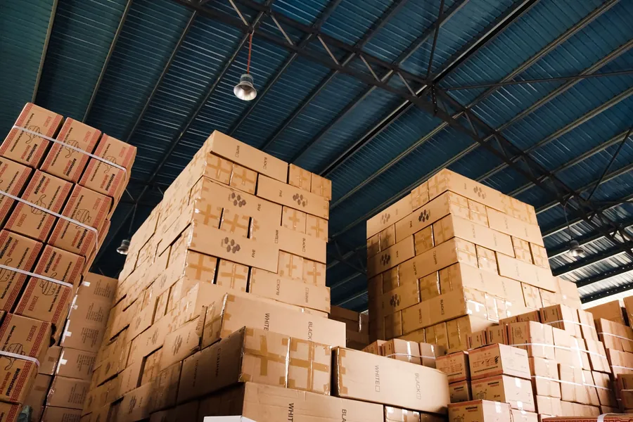 Warehouse stacked high with cardboard boxes of imported goods under a blue steel roof