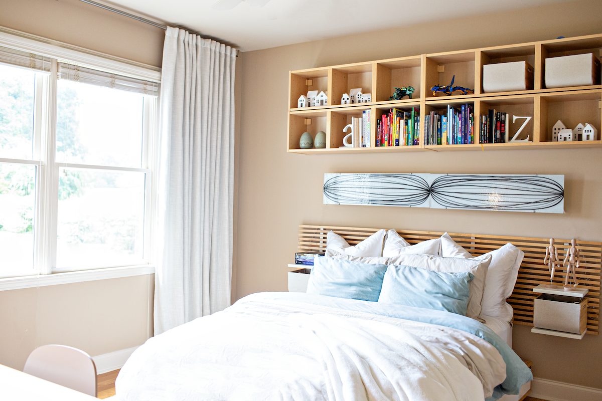 Boys’ room featuring a full size wooden bed with white and mint green bedding, and wooden bookshelves, next to a bright window with white floor-to-ceiling curtains.