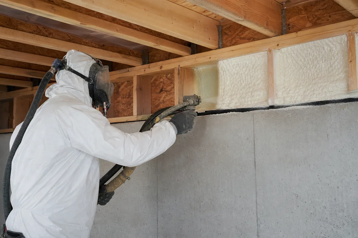 Installer applying spray foam insulation to basement rim joists