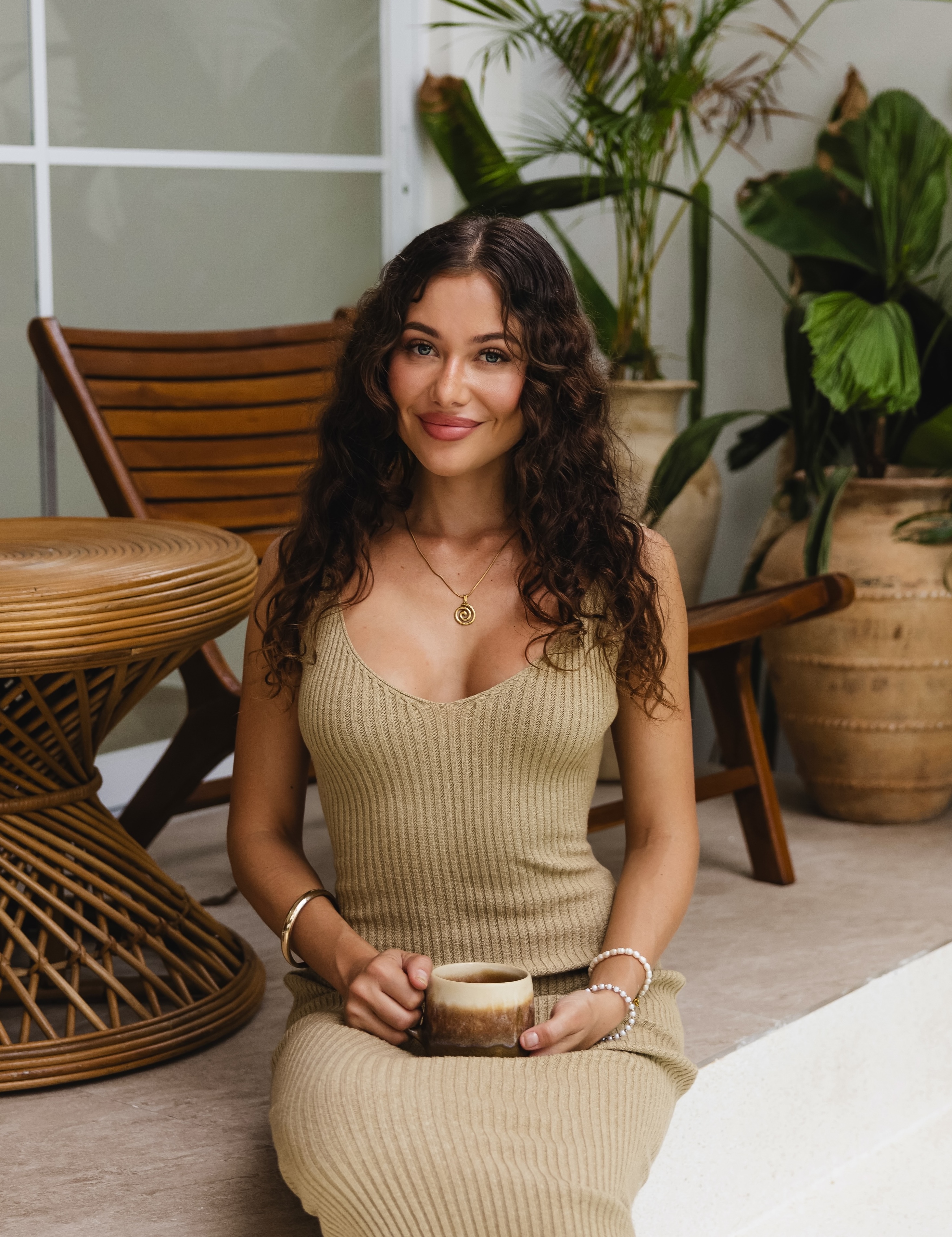 Ari seated with a coffee among tropical plants, smiling and at ease