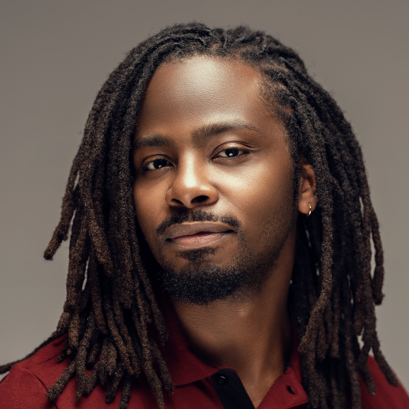 Man with locs on a dark red backdrop