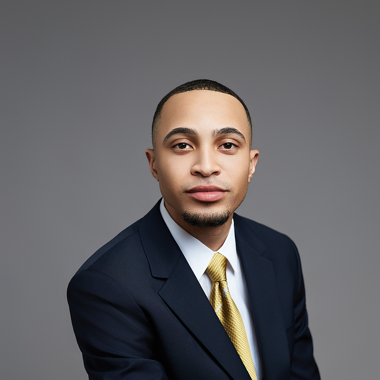 Man in a navy suit and gold tie on grey