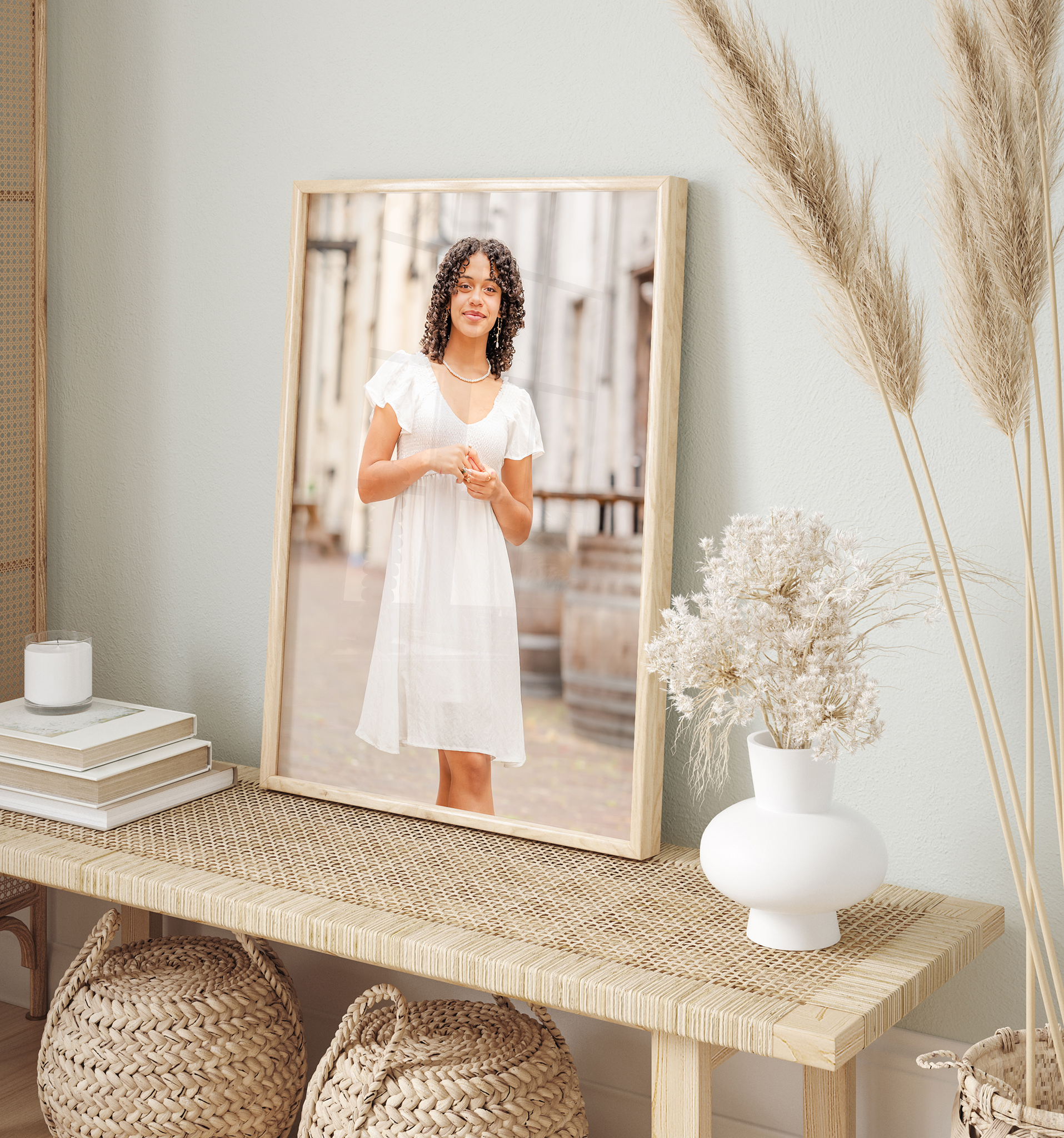 A senior portrait sits on a table in a home. The portrait features a high school senior wearing a short, flowy, white dress. She is standing in a street with white buildings behind her. The room is decorated in neutrals. Printed portraits are part of Virginia Beach photographer Justine Renee Photography's offerings.