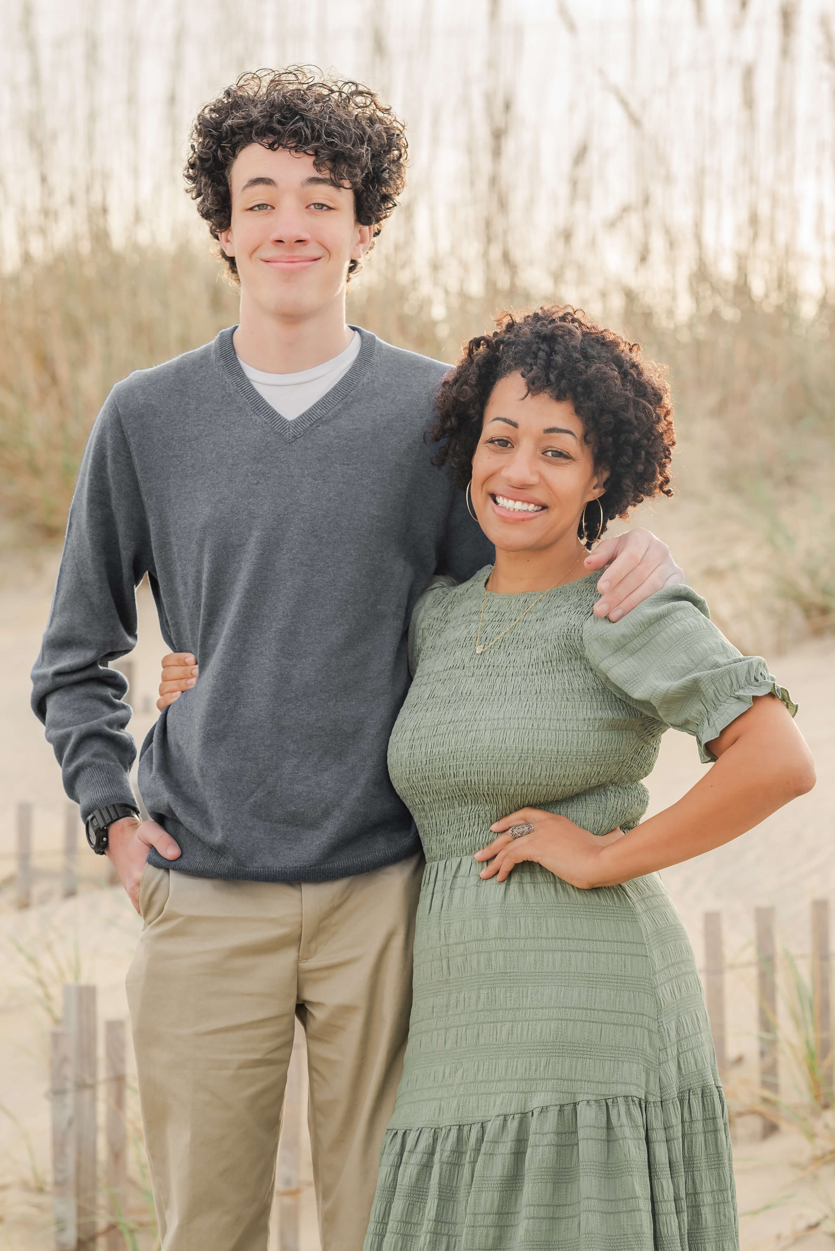 A mother in a green dress wraps her arm around her, very tall, teenage son The son is in a blue sweater and khakis.