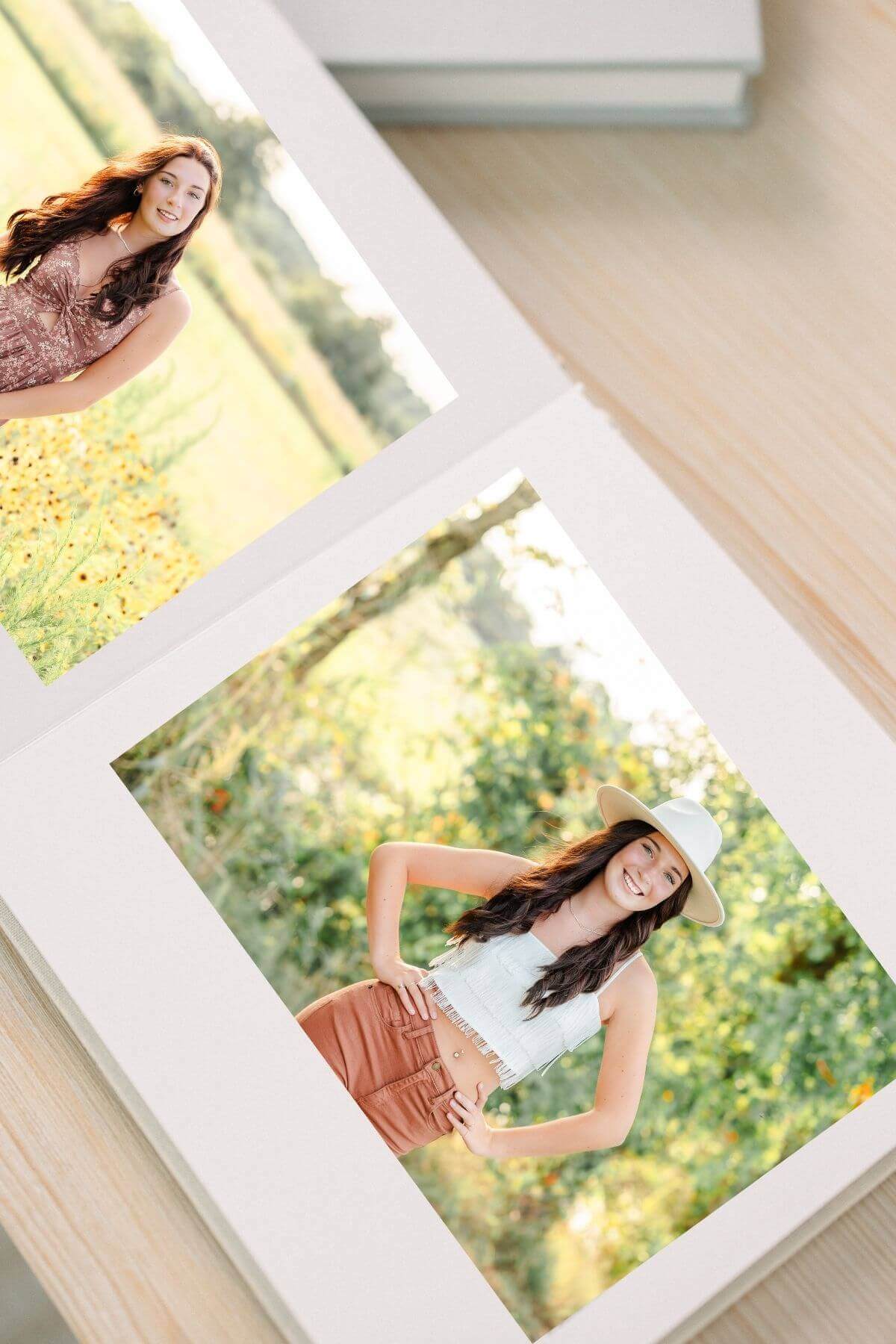 An heirloom album is open on a table. Displayed in the album are two images from a senior session in a bright, sun-filled field.