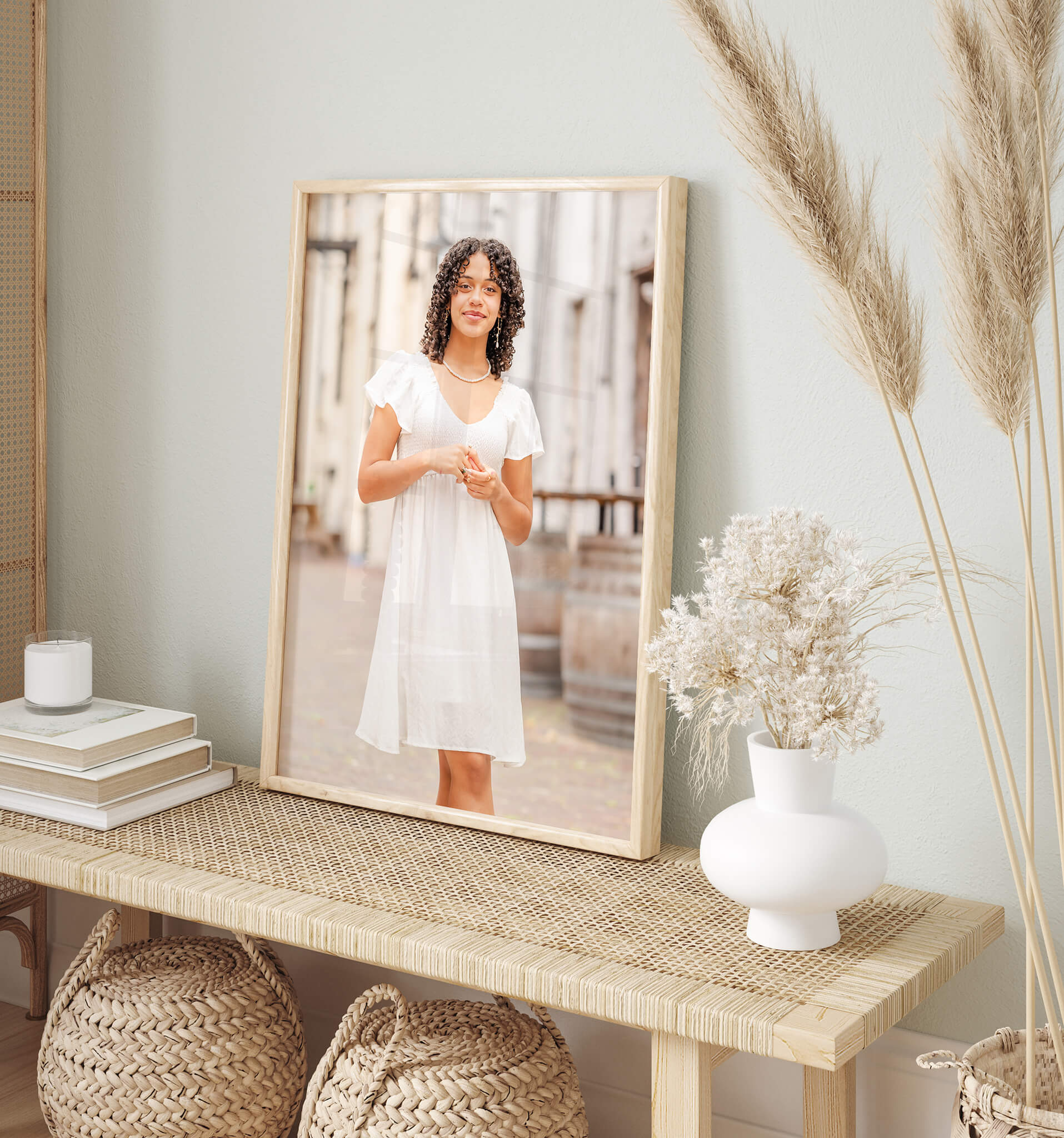 A photo of a high school senior in a white dress, sits on a table. The room is decorated in neutrals which compliments her outfit.