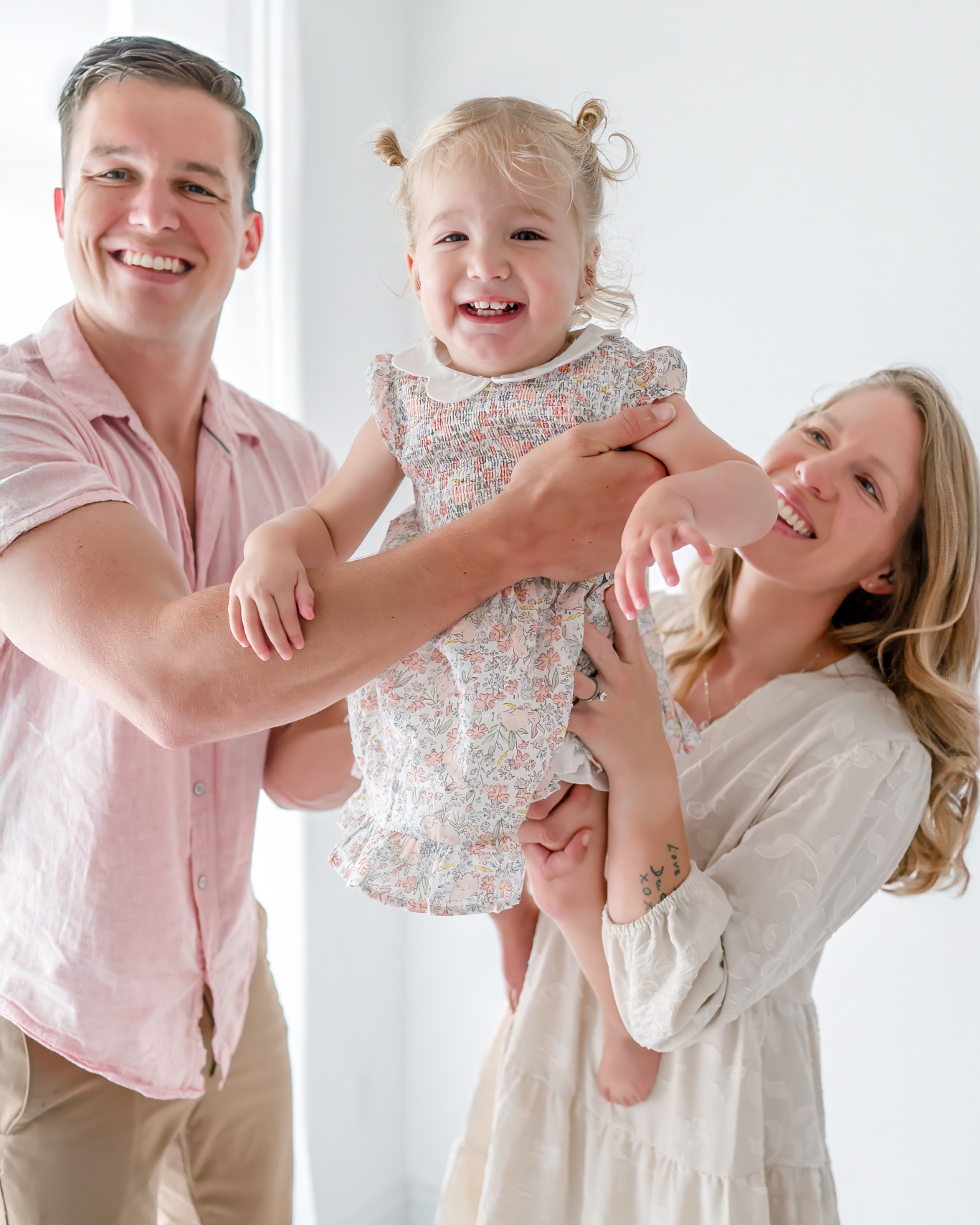 A mother and father swing their toddler daughter between them. She is laughing as they hold her up.
