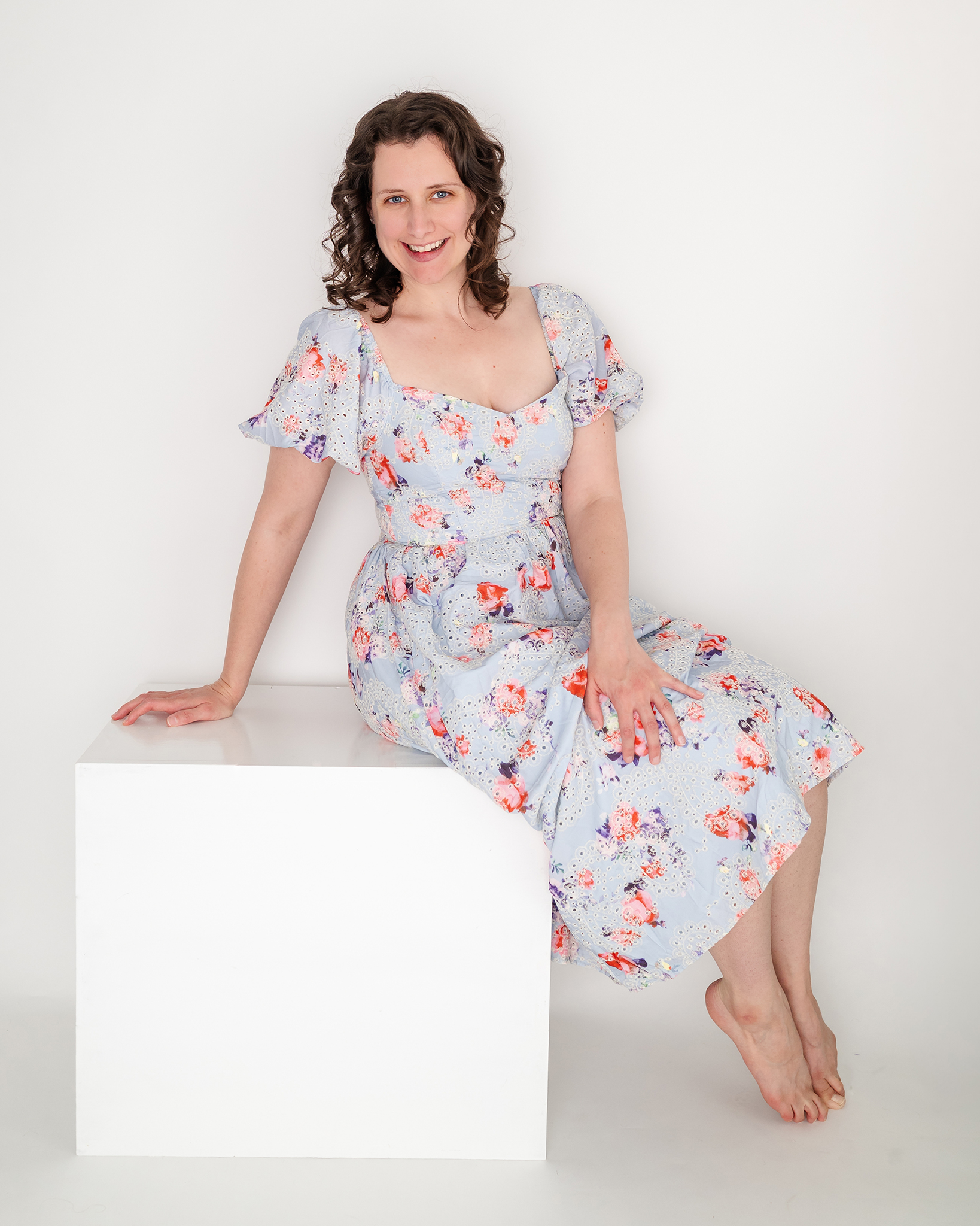Chesapeake photographer, Justine Renee Photography is pictured. She is wearing a a blue floral dress and pictured in a clean white set.