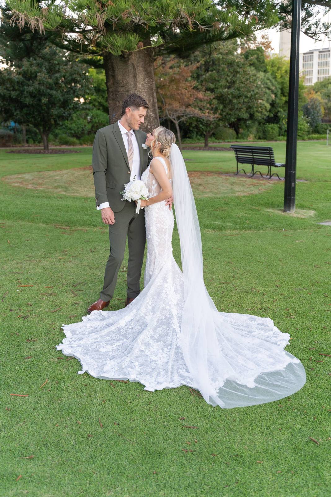 Couple on a green lawn with a long lace train spread behind the bride