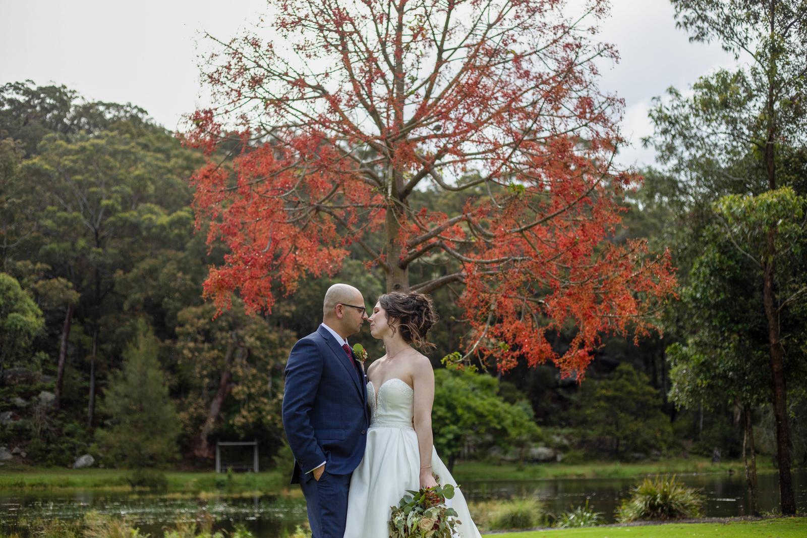 Couple beneath a flowering red tree beside a pond