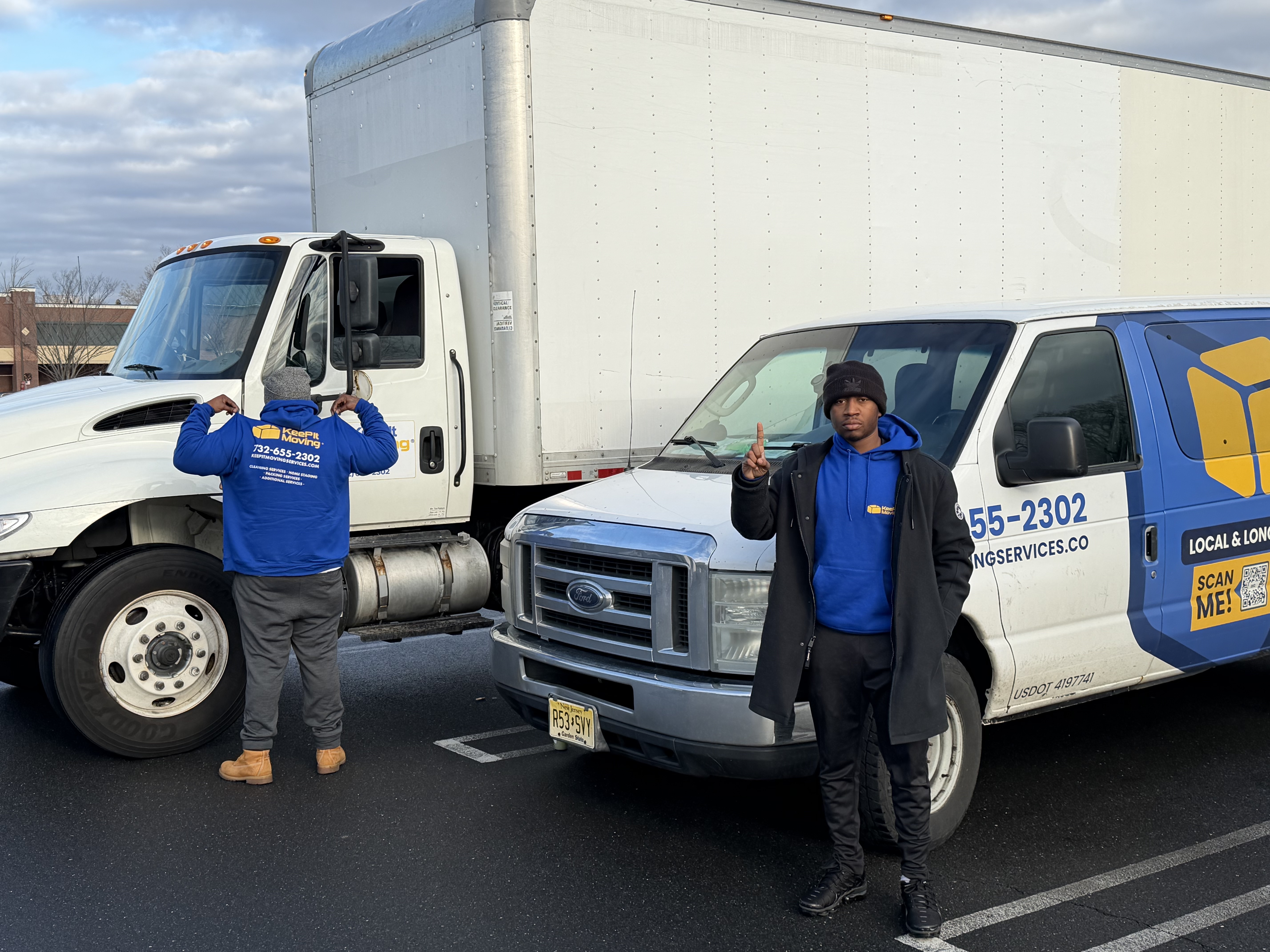 Two Keep It Moving Services crew members in branded hoodies standing in front of a box truck and van