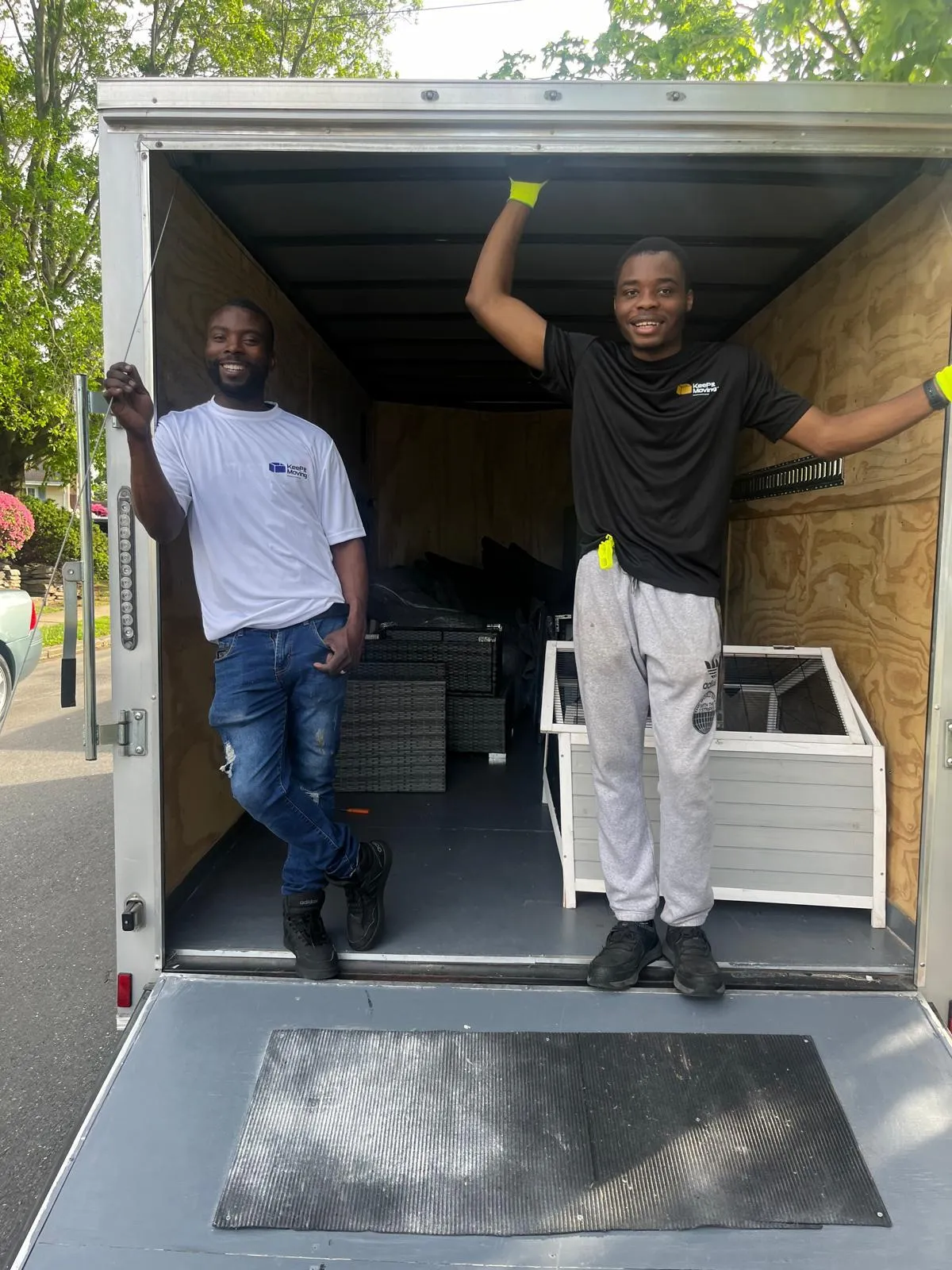 Two Keep It Moving Services crew members in a cargo trailer, smiling, moving a wrapped cabinet