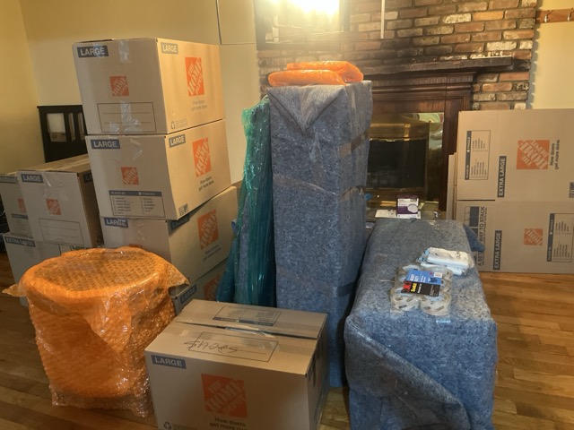 Living room staged with moving boxes and wrapped furniture near a brick fireplace — ready for a KIMS residential move in NJ