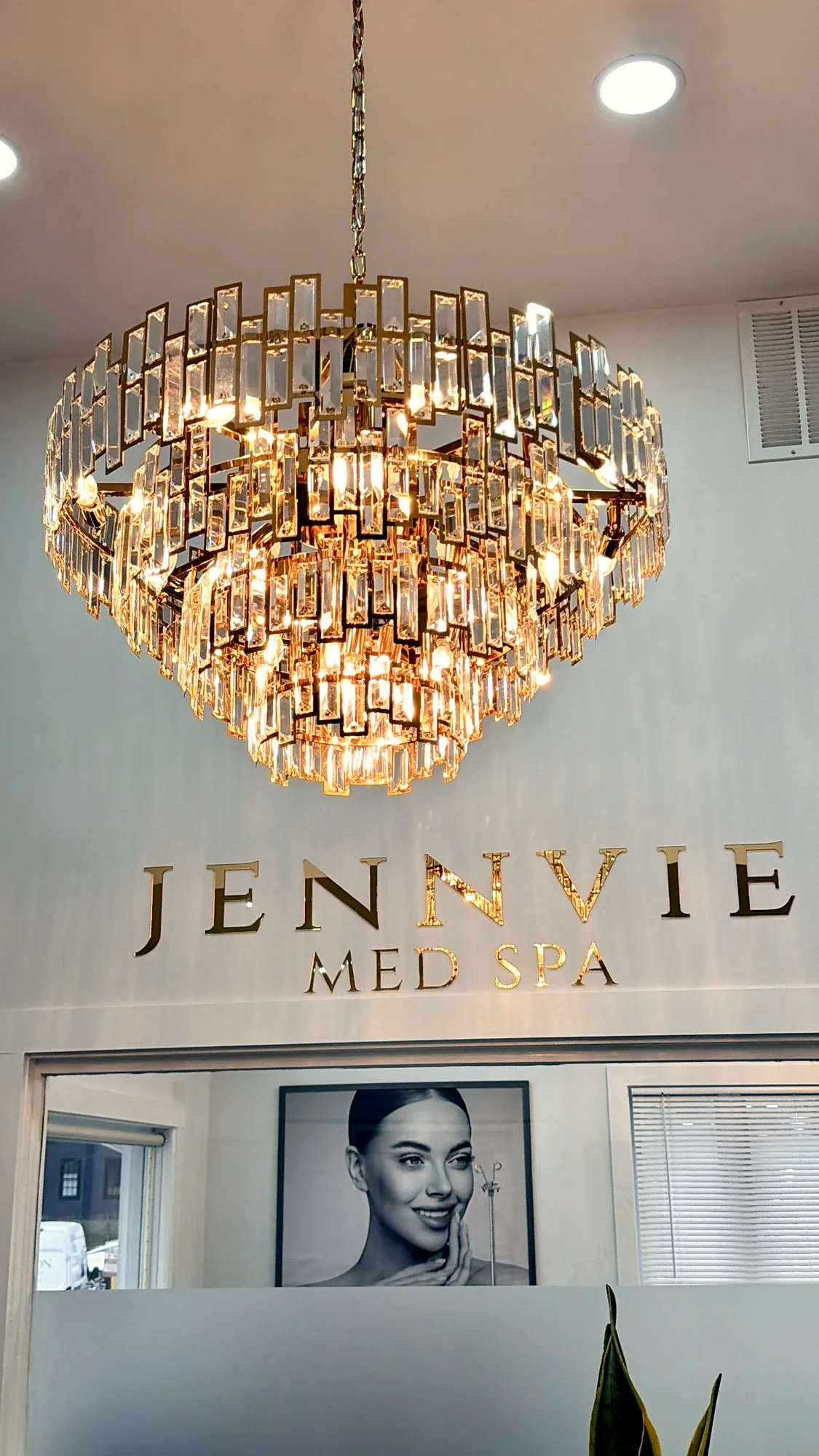 Crystal chandelier above the gold JENNVIE Med Spa wall letters in Westport, CT