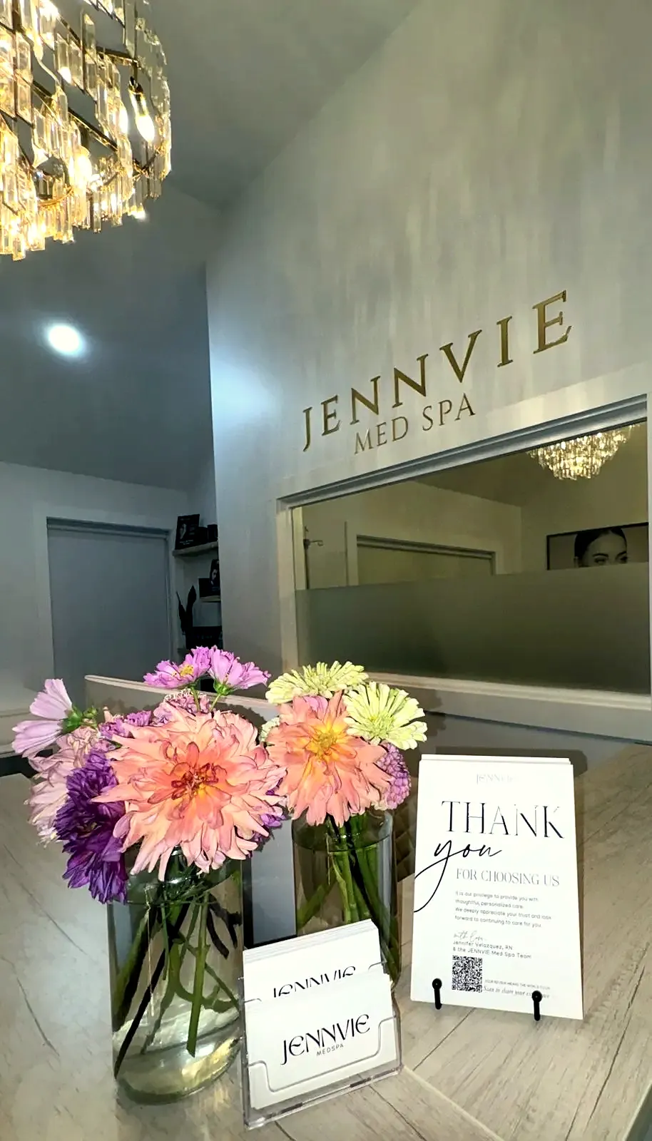 Reception at JENNVIE Med Spa in Westport, CT with the gold wall sign, crystal chandelier and fresh flowers