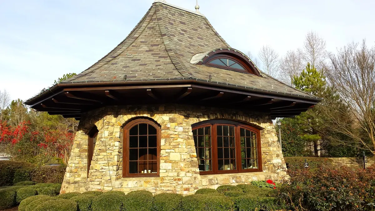 Stone building with flared shingle roof and dark wood arched windows