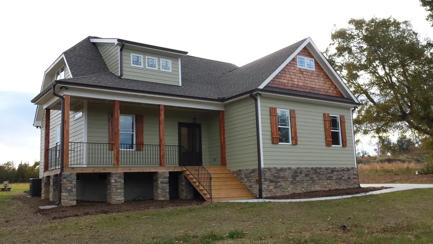 Two-story green sided home with porch and reddish brown shutters