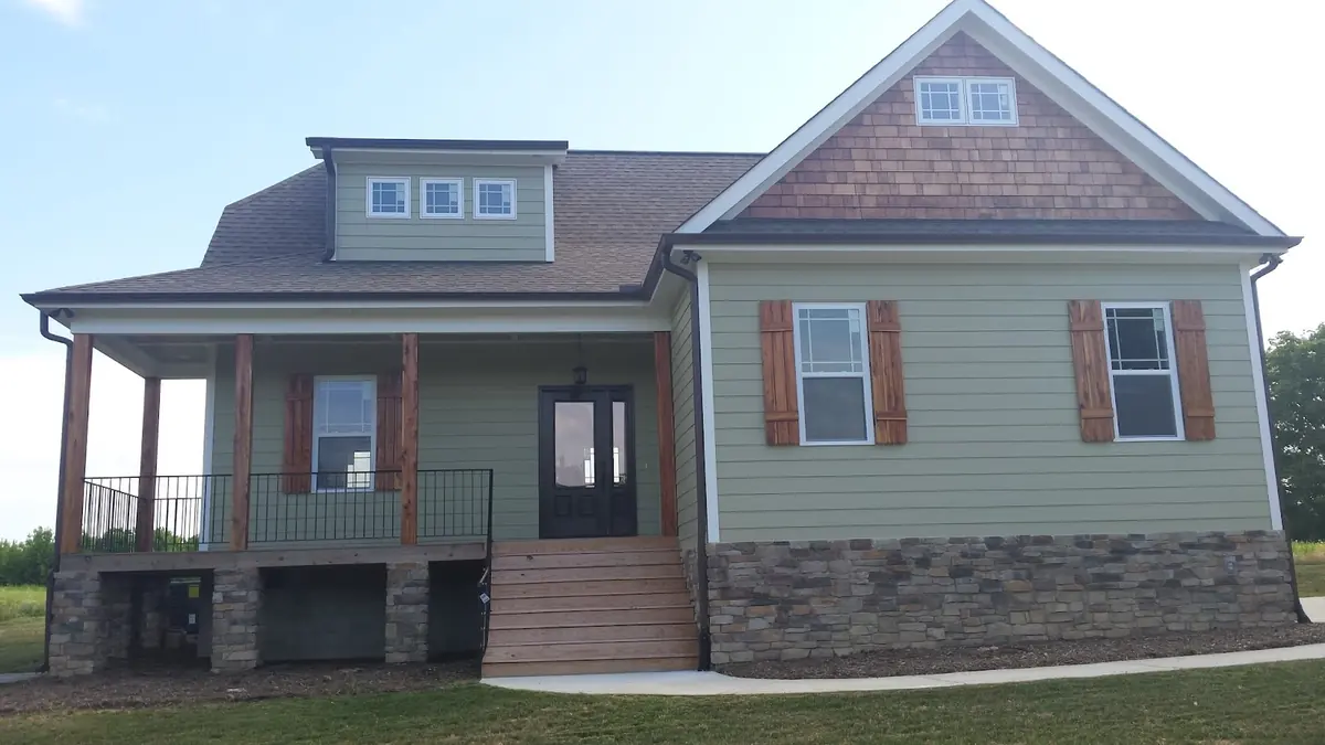 Sage green home with stone veneer foundation and wooden porch posts