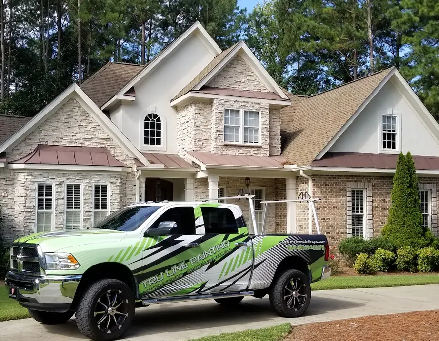 Tru-Line Painting truck with lime green and black wrap parked in front of a large stone and brick home
