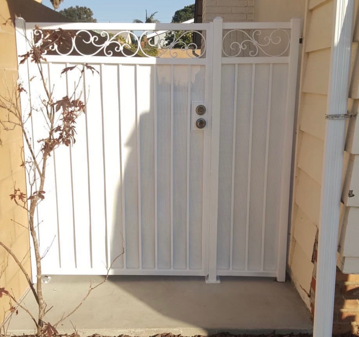 White ornamental pedestrian gate with scrollwork at a side yard entrance