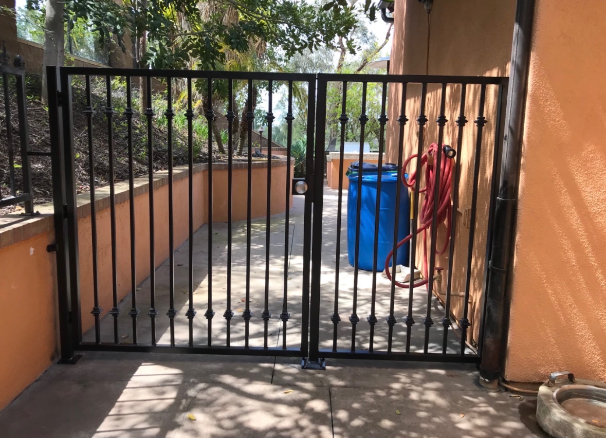 Black iron double pedestrian gate with finials at a courtyard entrance