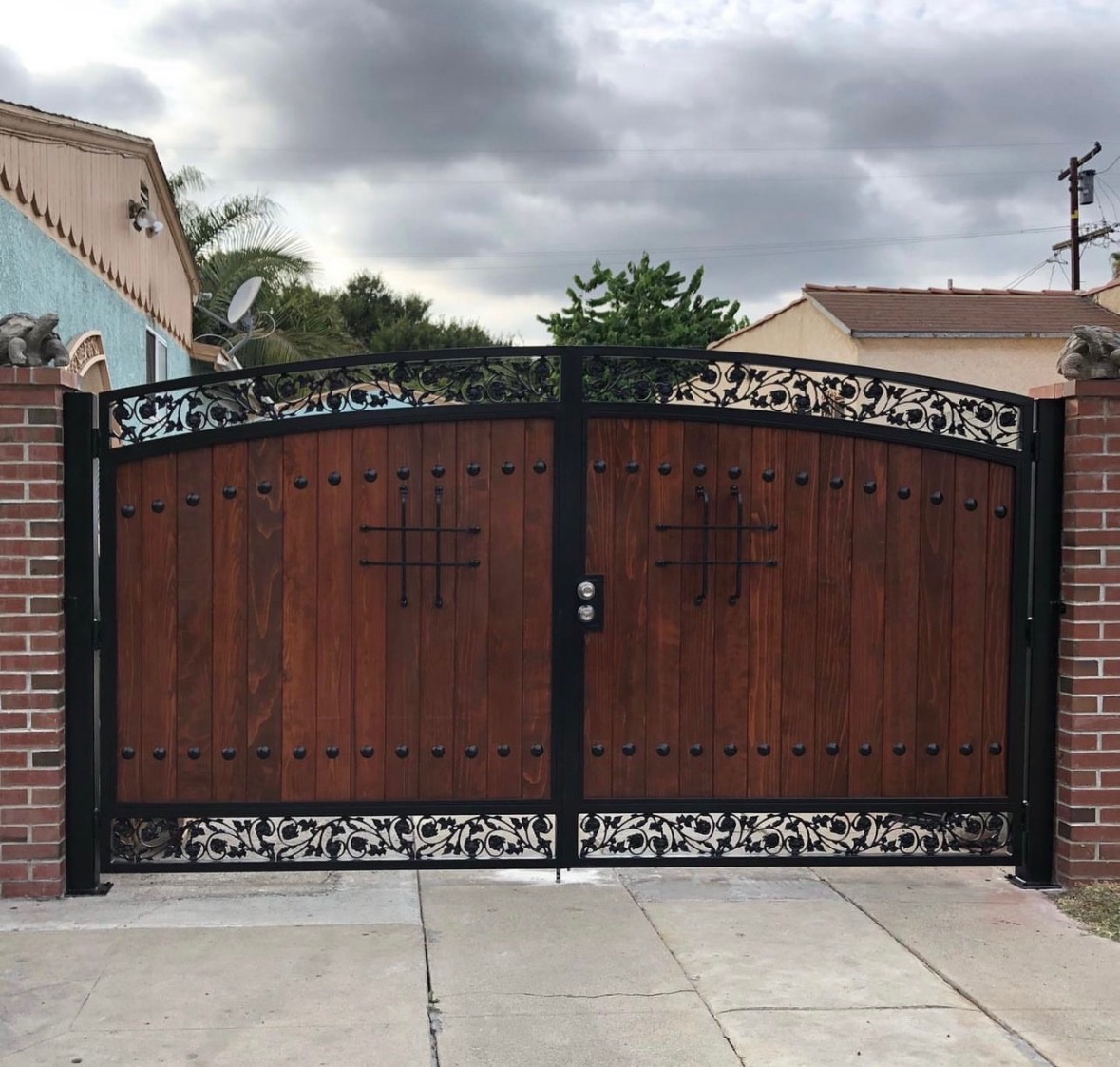 Custom wood and iron driveway gate with scrollwork between brick columns