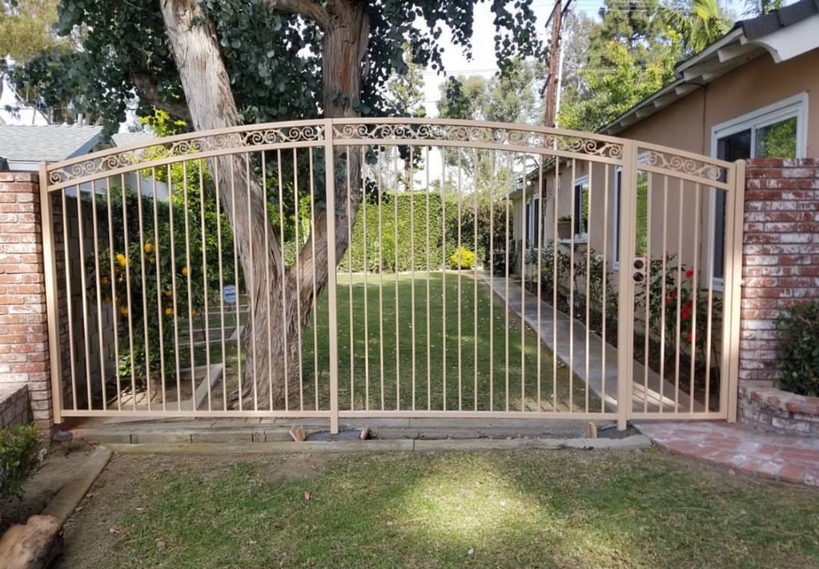 Tan ornamental arched double driveway gate with scrollwork and brick columns