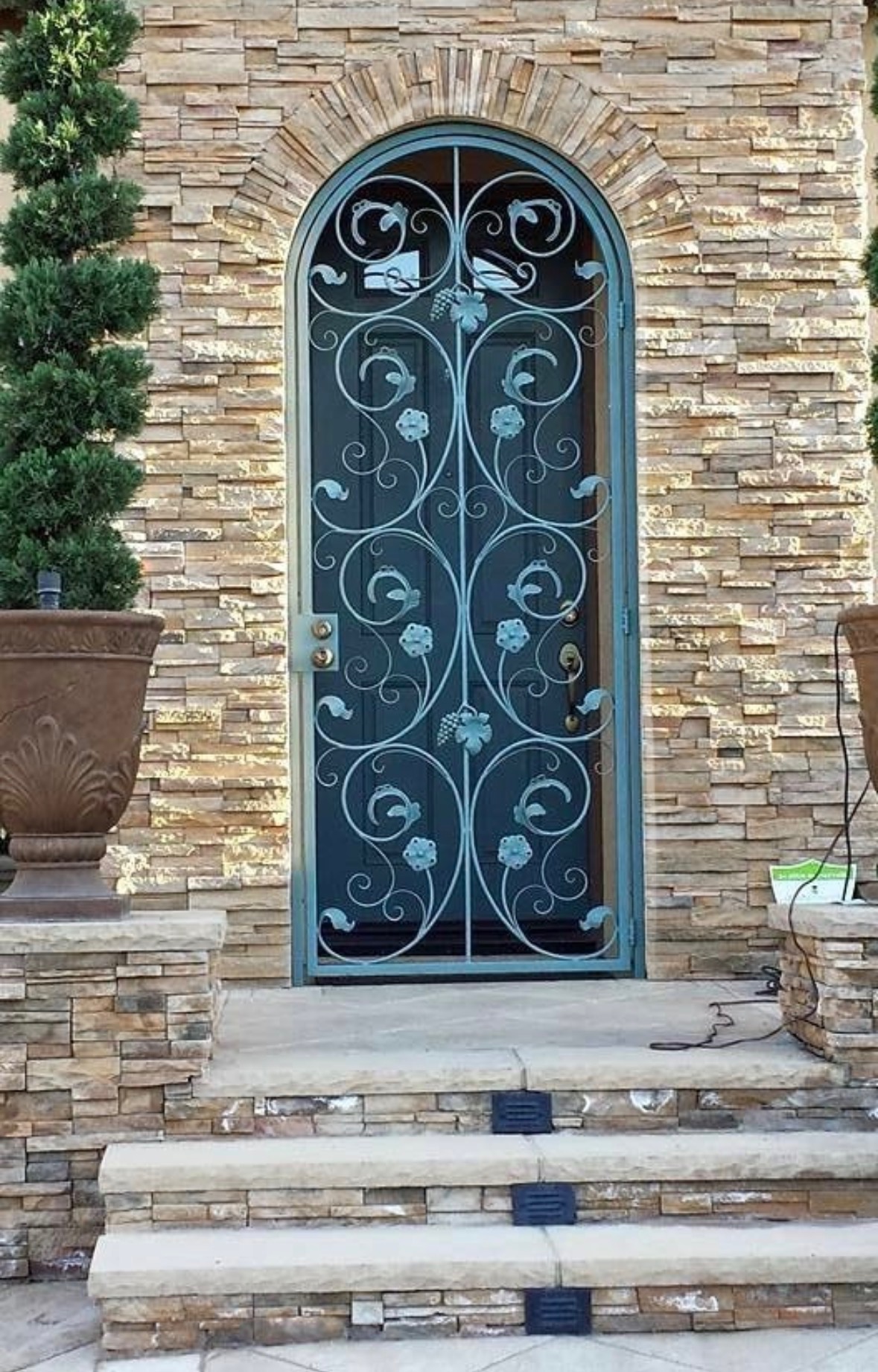 Custom ornamental iron door in a verdigris finish on an arched stone facade