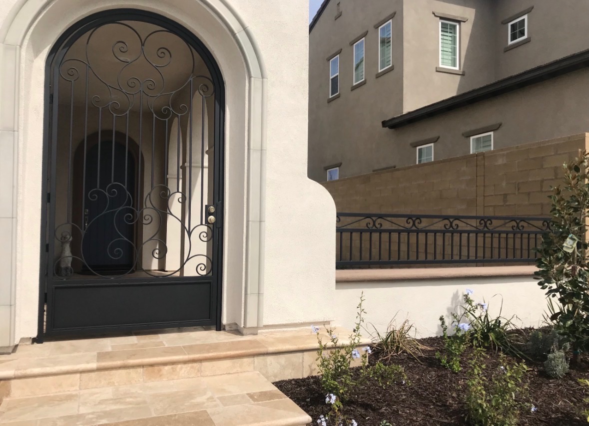 Custom ornamental arched iron door with scrollwork on a luxury stucco home
