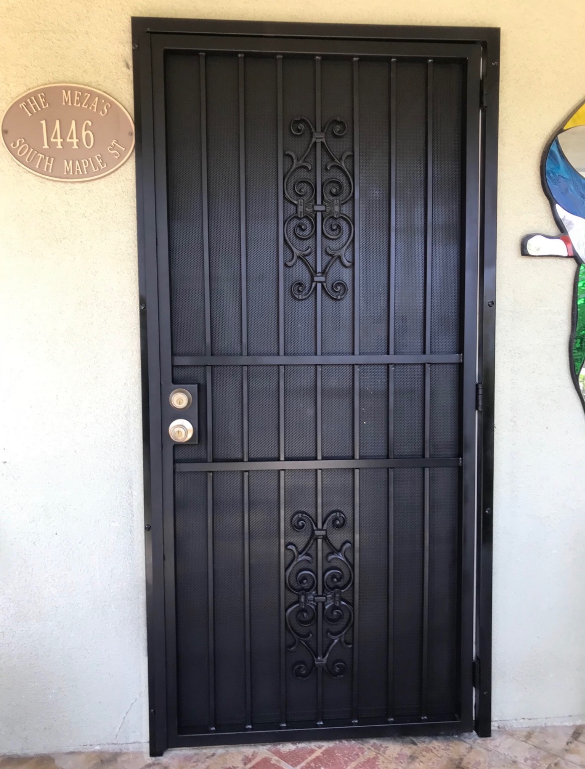 Black iron security screen door with scrollwork at a residential entrance
