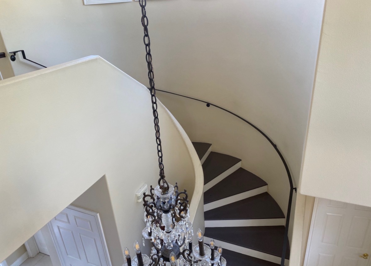 Curved iron handrail on a winding staircase beneath a chandelier