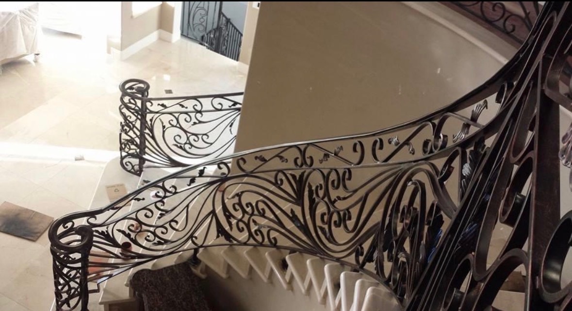 Ornate black wrought iron curved staircase railing with marble floor