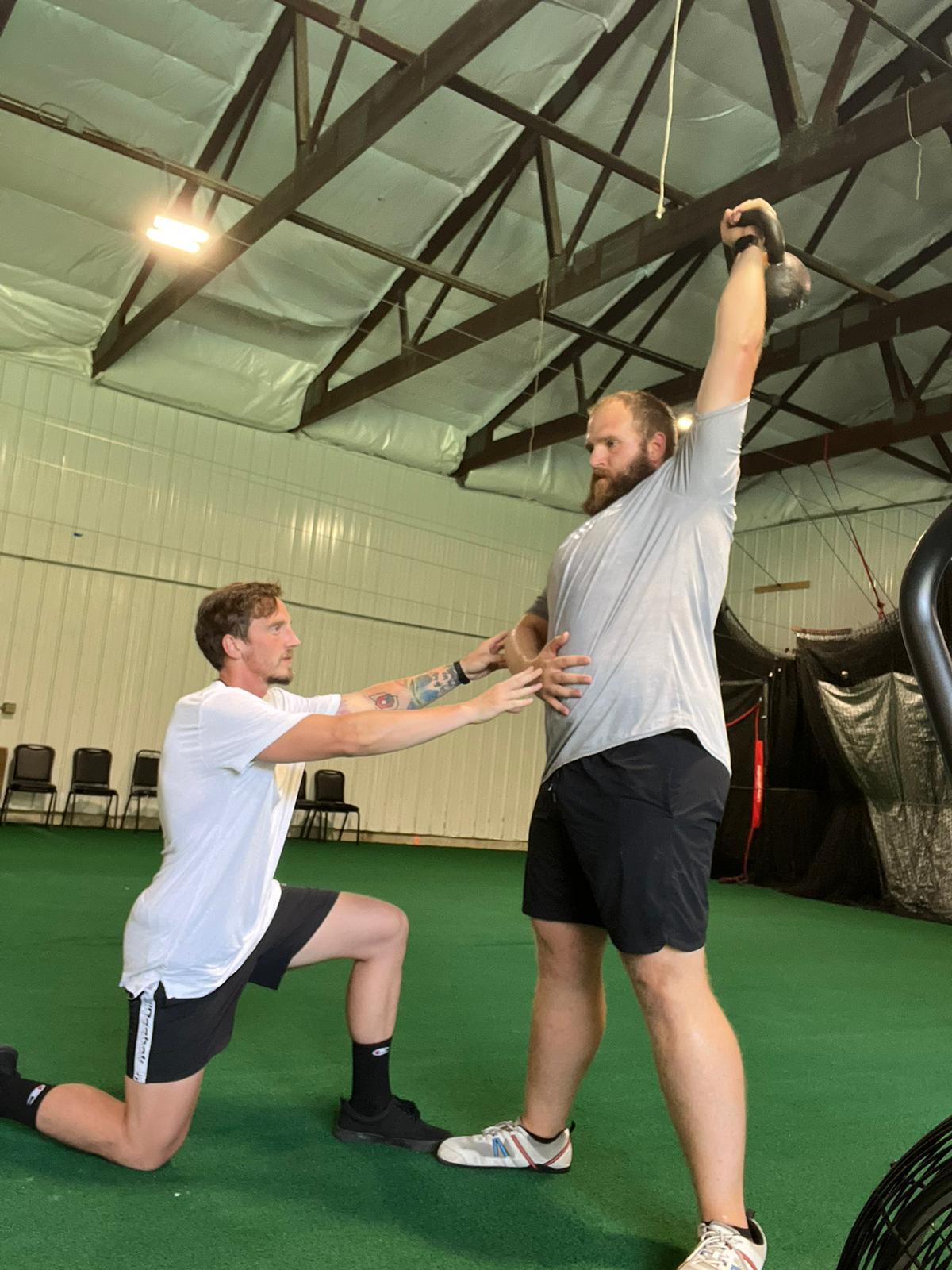 A coach cueing breathing mechanics during an overhead kettlebell lift