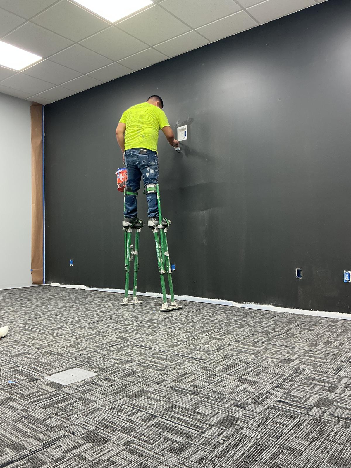 Painter on drywall stilts working on a dark accent wall