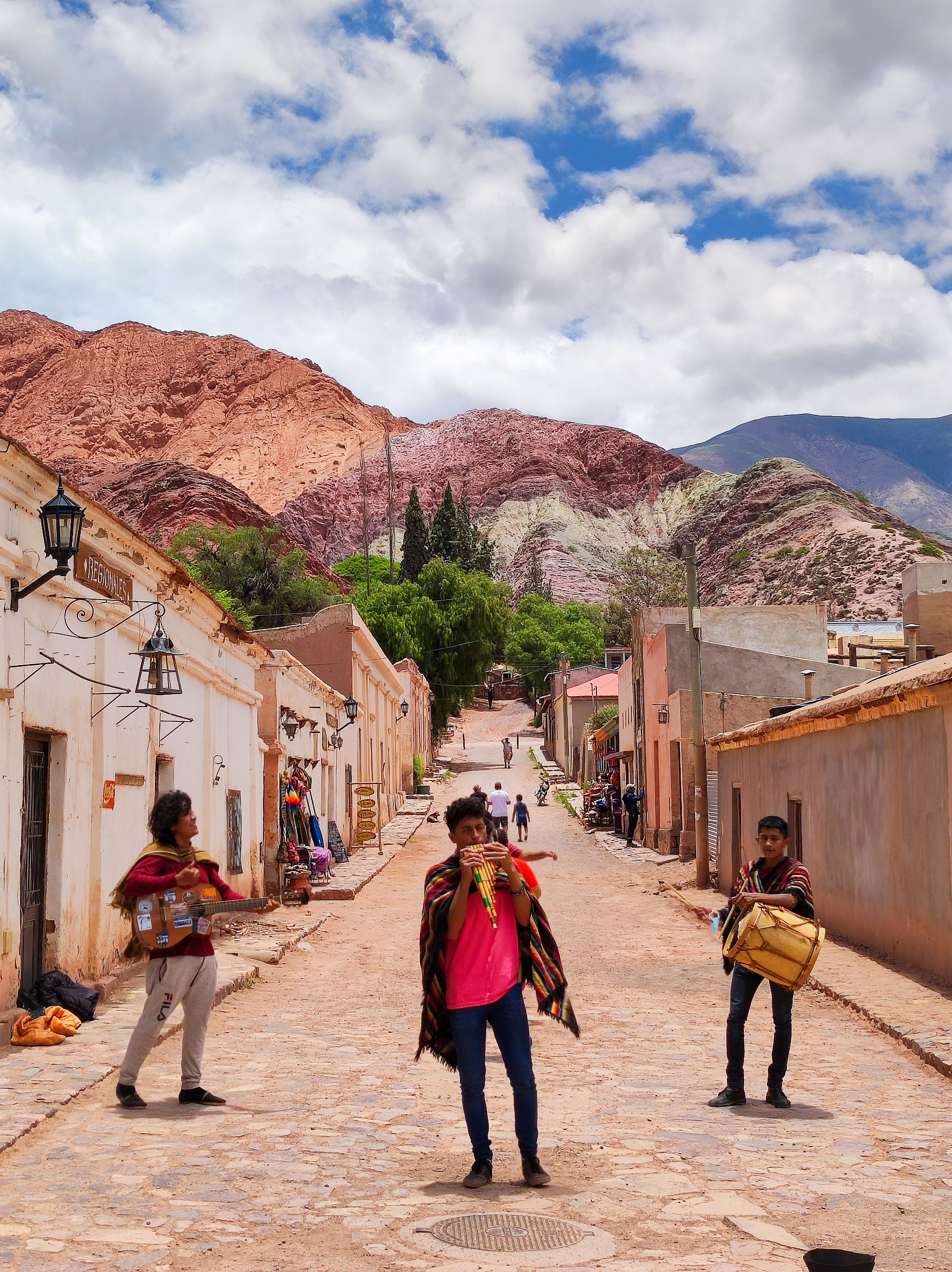 Músicos callejeros en la vibrante Tilcara, Argentina, con colinas coloridas y arquitectura tradicional.
