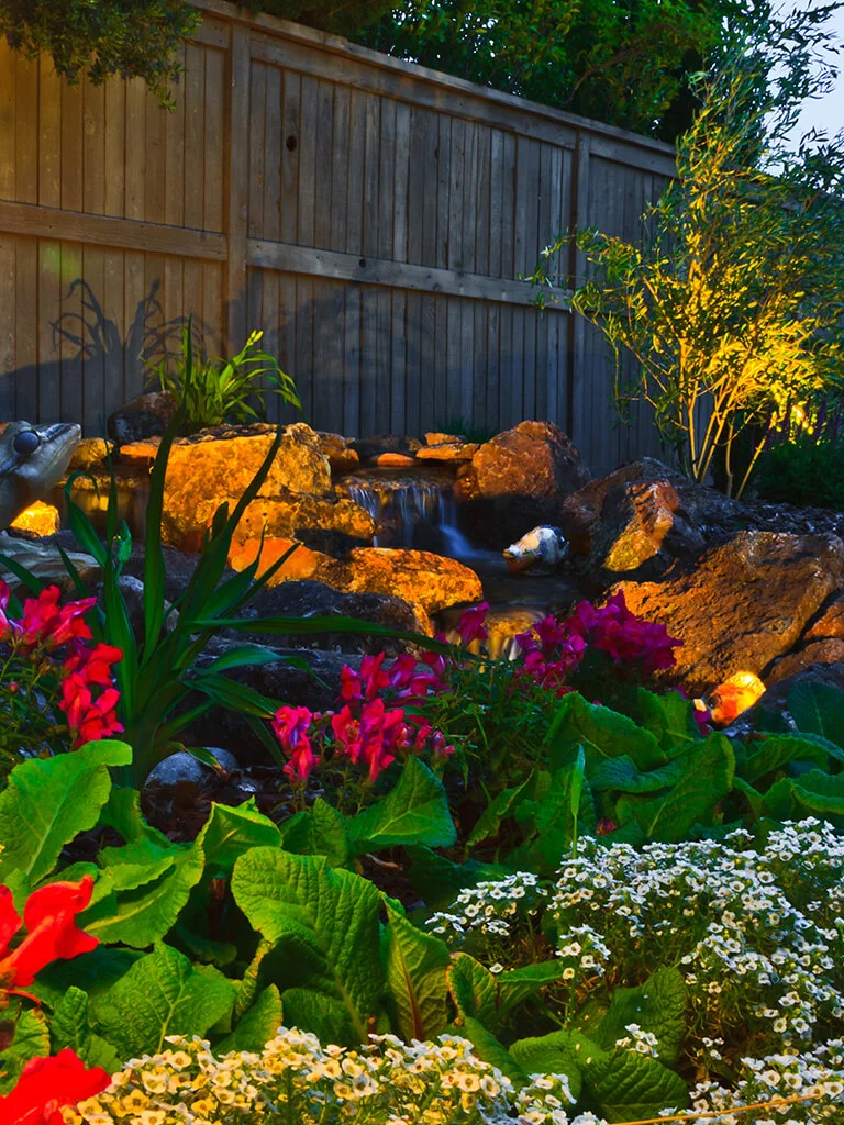 Illuminated waterfall, boulder accents, and landscape lighting by Lavish Gardens Landscape