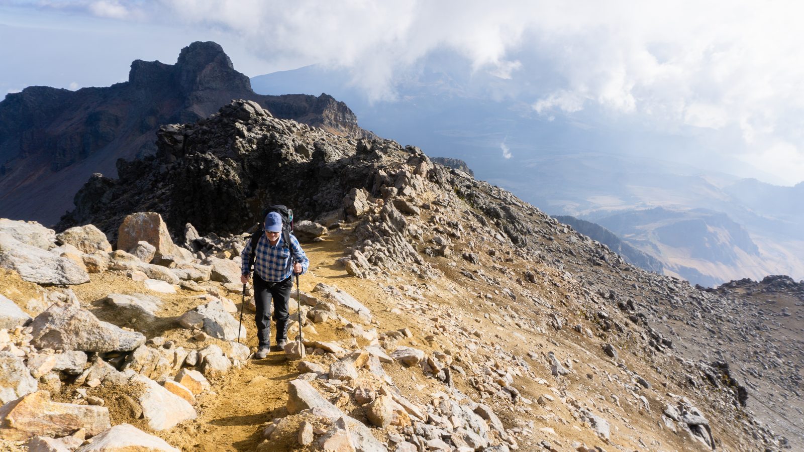 Client walking uphill with a pack and poles on the Iztaccihuatl trail