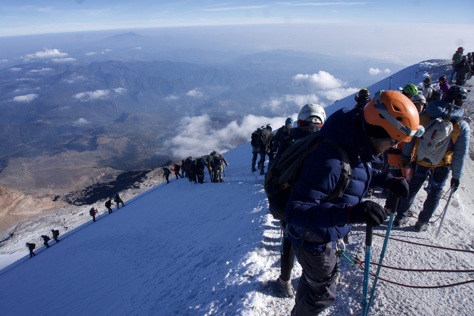A long roped line of climbers ascending the Jamapa glacier on Pico de Orizaba above a sea of clouds