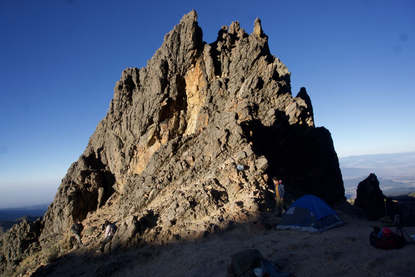 Tents pitched below a golden rock tower on Iztaccíhuatl in late afternoon light