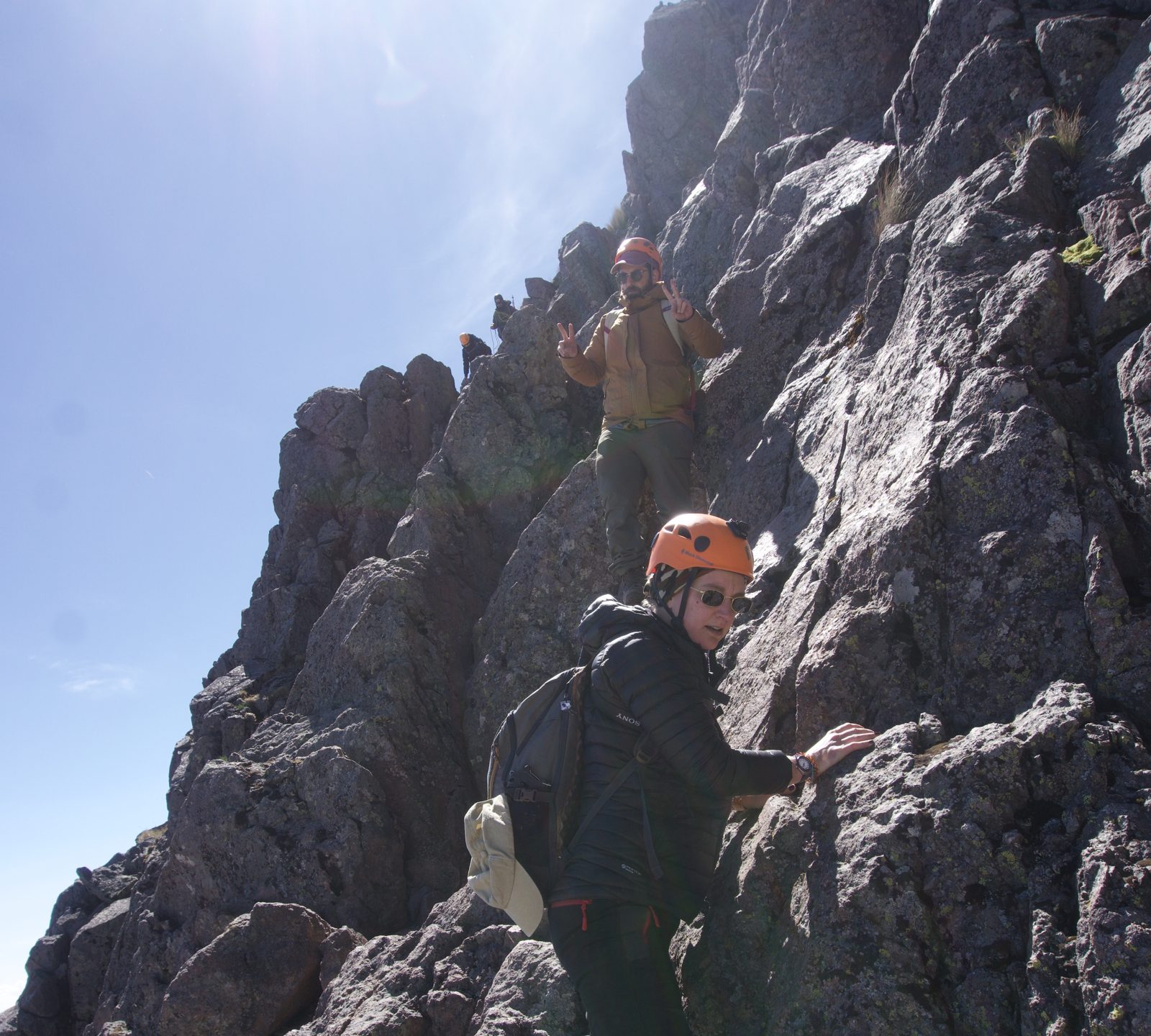 A climber in an orange helmet scrambling up a rock ridge on Iztaccíhuatl against the sun