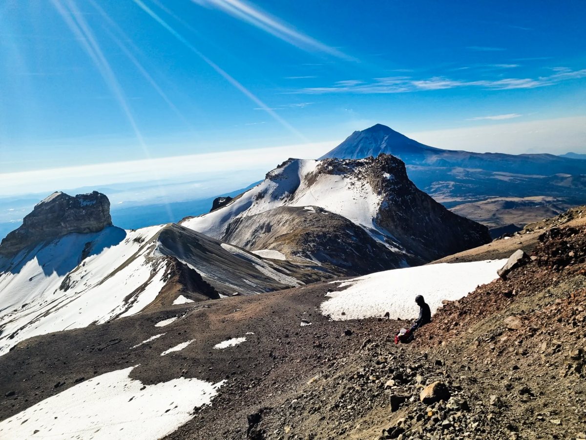 A climber resting high on Iztaccihuatl with Popocatepetl behind