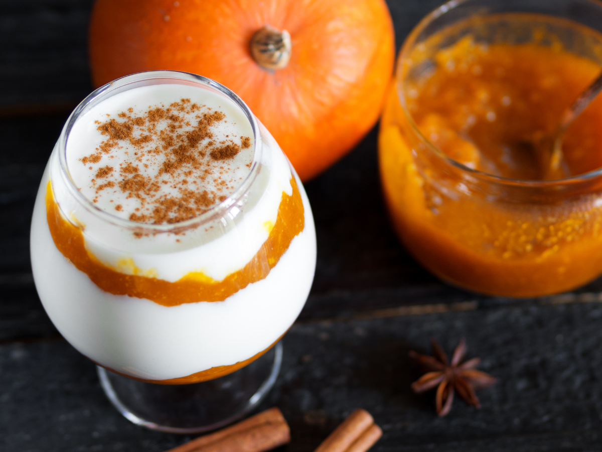 A glass of layered pumpkin and yogurt topped with cinnamon, beside a pumpkin and a jar of pumpkin puree. A glass of layered pumpkin and yogurt topped with cinnamon, beside a pumpkin and a jar of pumpkin puree.